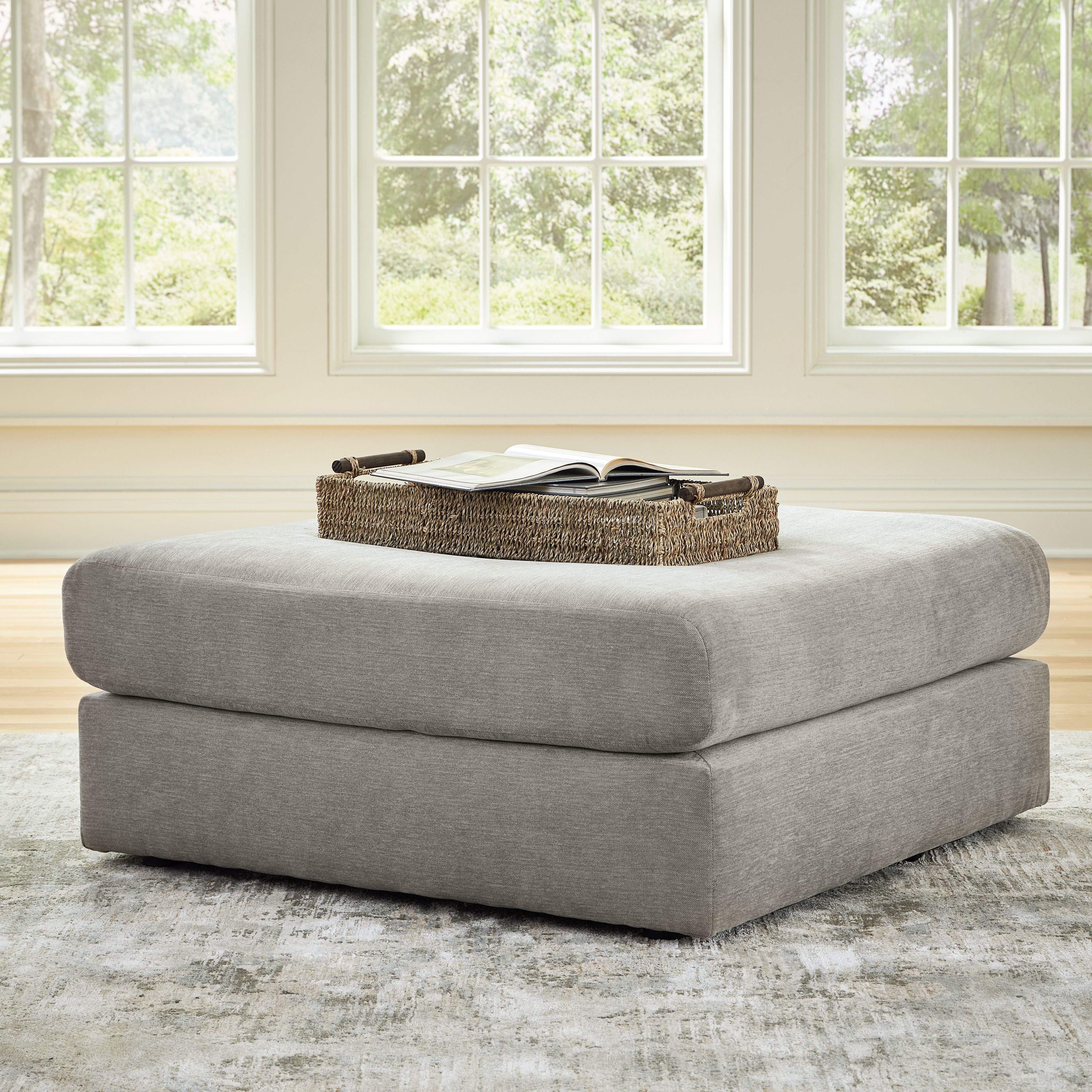 Upholstered ash-gray ottoman with rounded corners; open book on top
