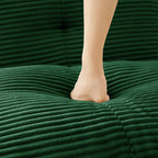 Green corduroy sectional chaise cushion with foot resting on the upholstered surface