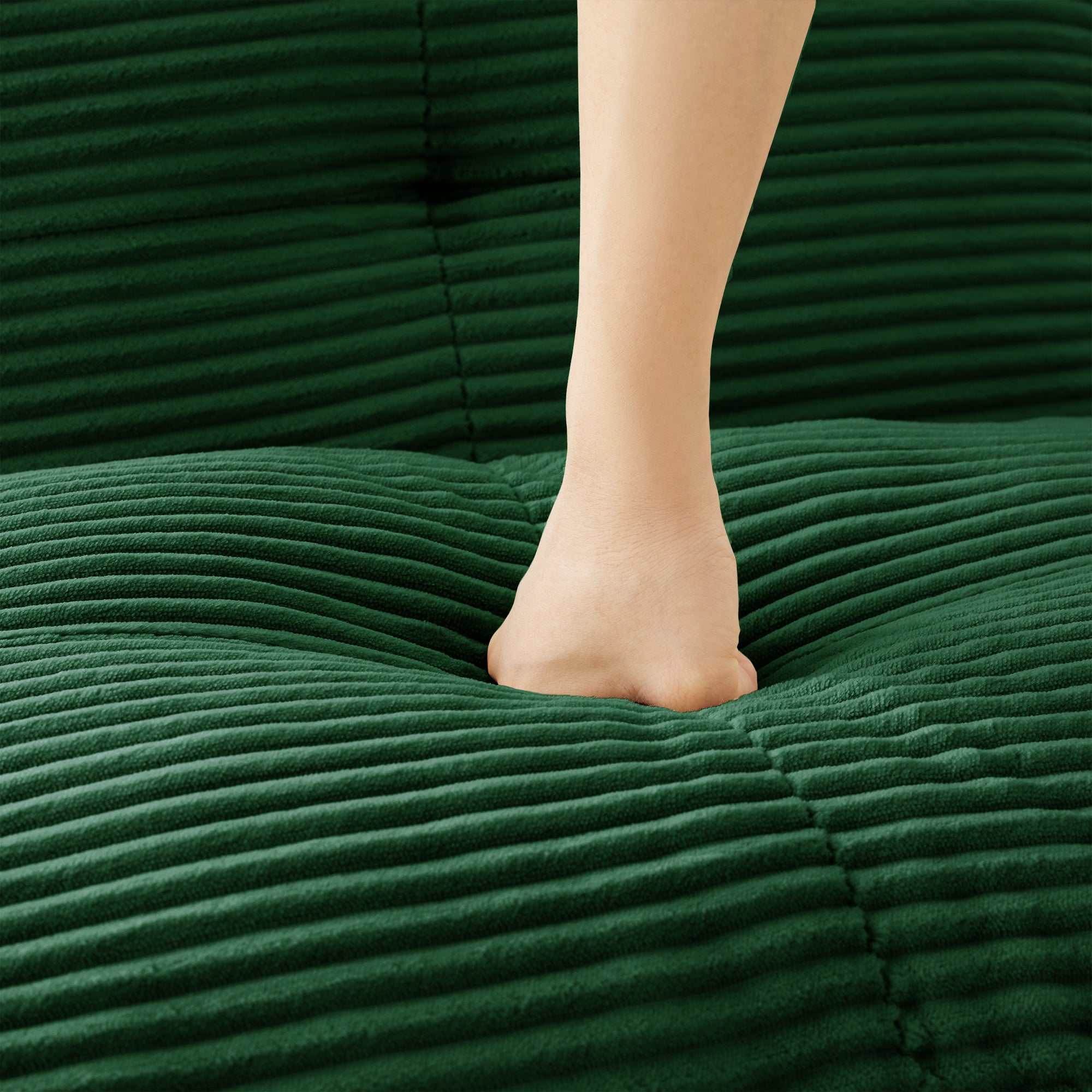 Green corduroy sectional chaise cushion with foot resting on the upholstered surface