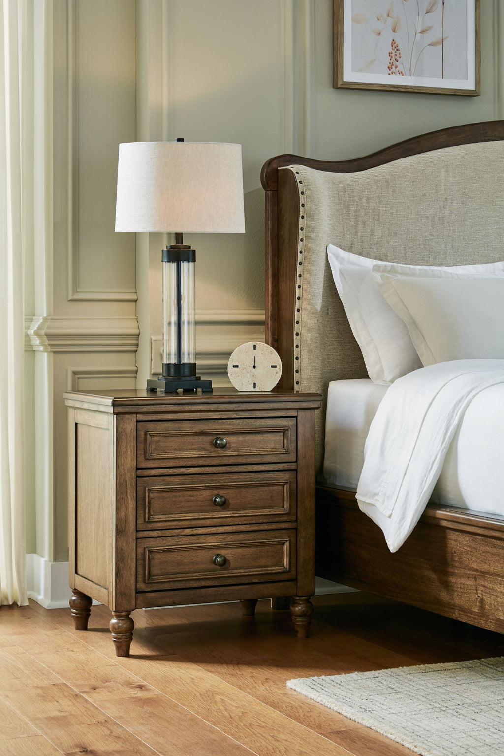 Brown three-drawer night stand with lamp and three drawers beside a bed