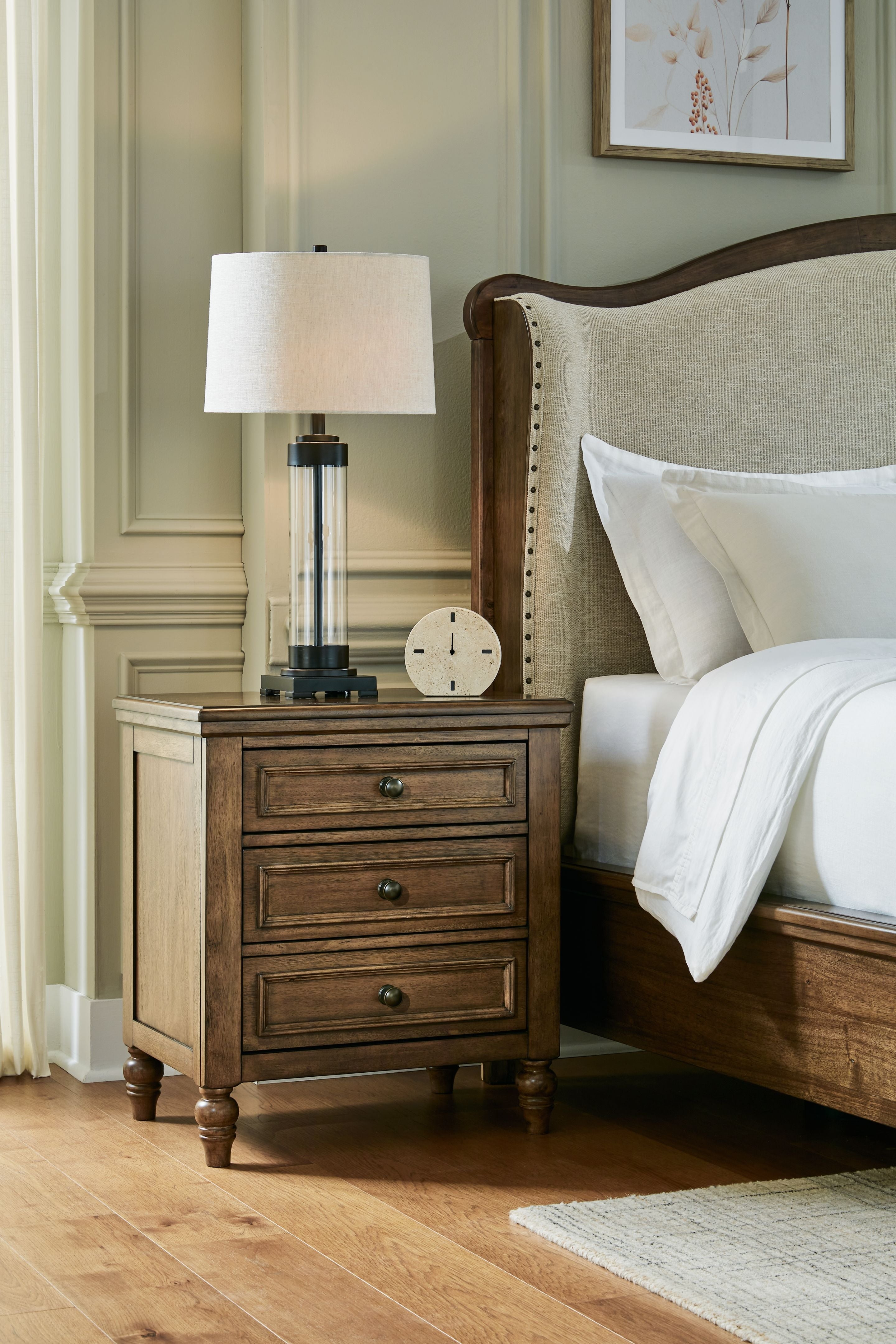 Brown three-drawer night stand with lamp and three drawers beside a bed