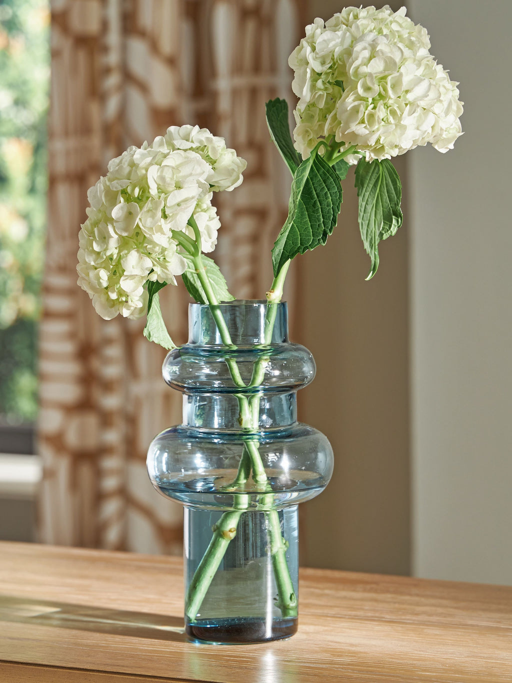 Blue glass bud vase holding white hydrangea-style flowers