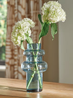 Blue glass bud vase holding white hydrangea-style flowers