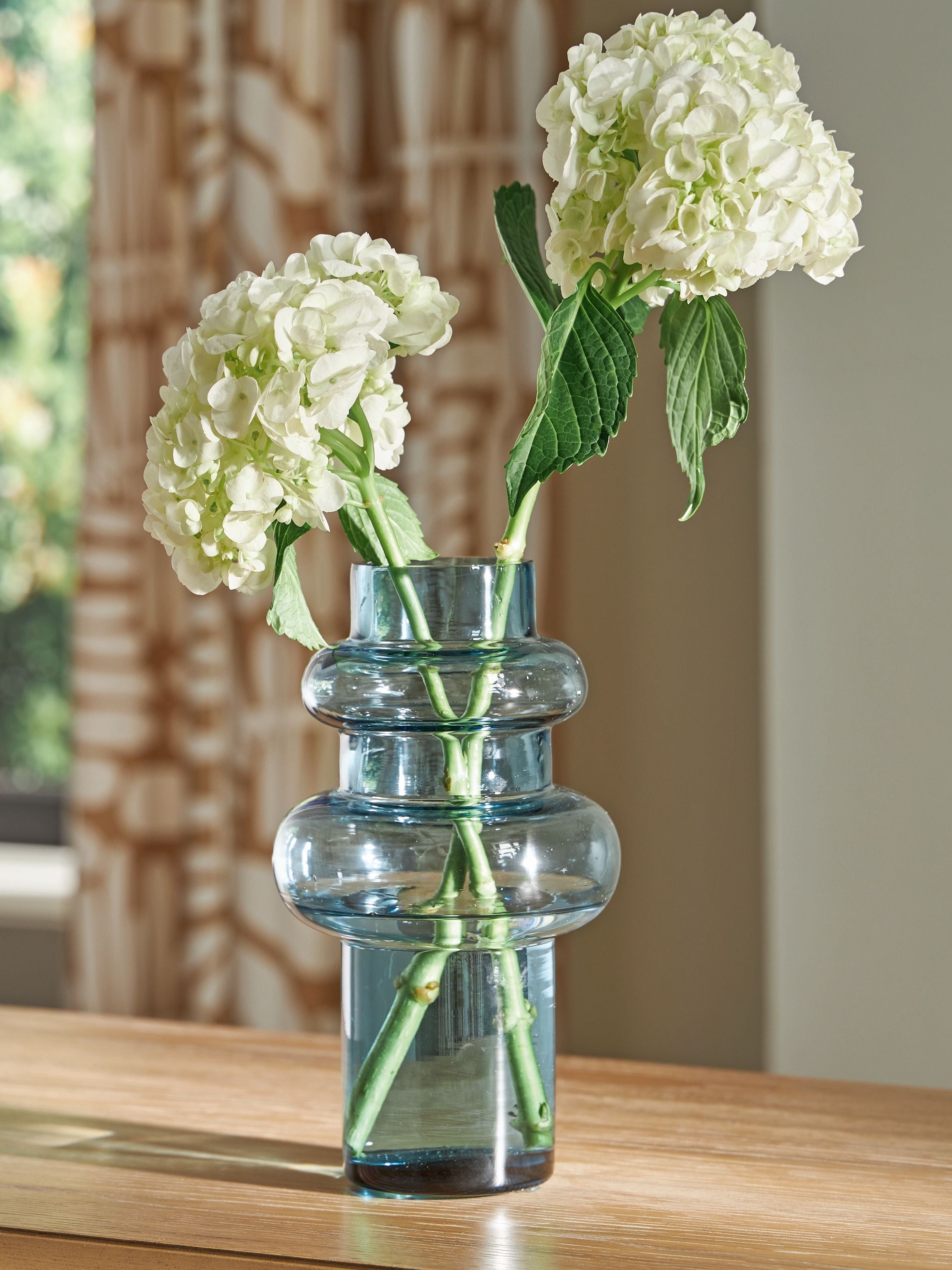 Blue glass bud vase holding white hydrangea-style flowers