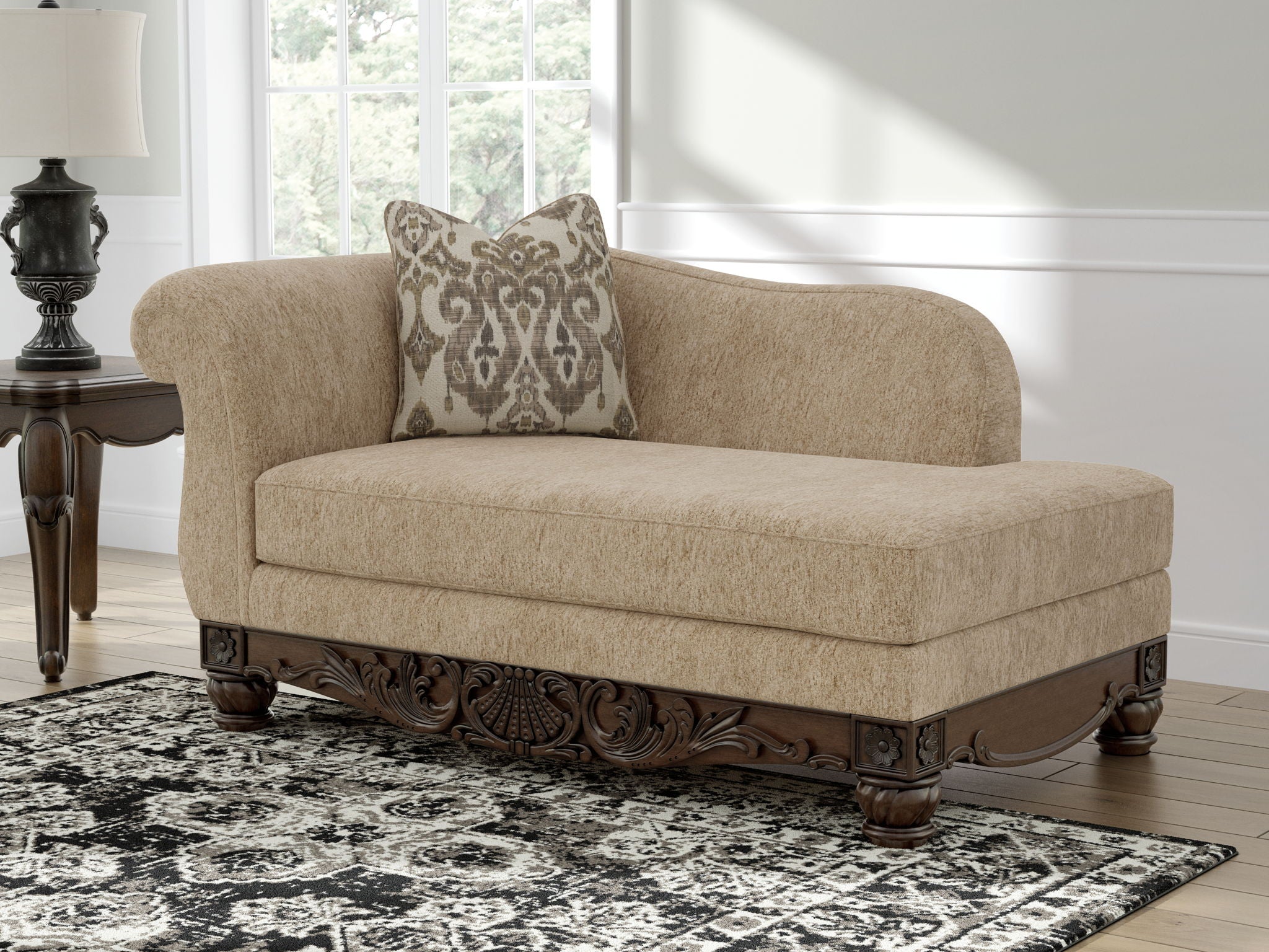 Beige corner chaise with patterned pillow and dark carved wooden base, front view.