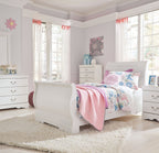 White sleigh bed with rounded headboard, styled with pink quilt and blue floral pillows.