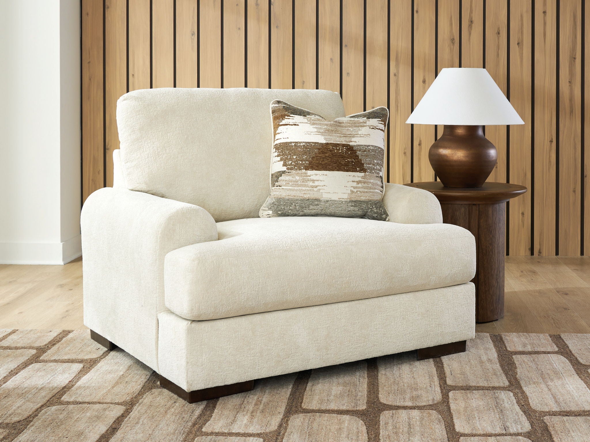 Beige armchair with wide arms, patterned throw pillow, and simple dark legs