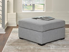 Oversized pewter gray ottoman with padded top and black legs, angled view