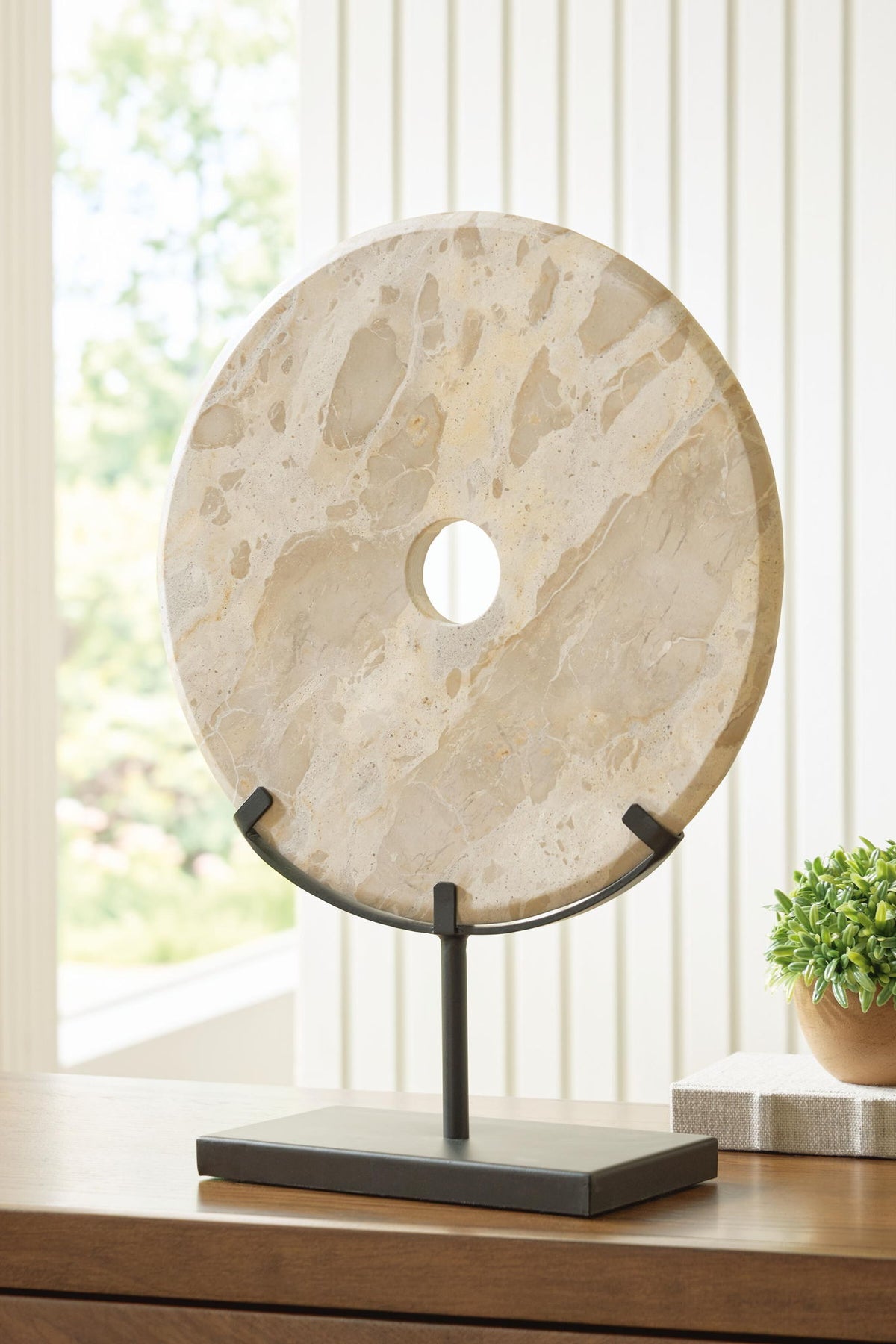 Light beige circular stone sculpture with central hole on dark rectangular base