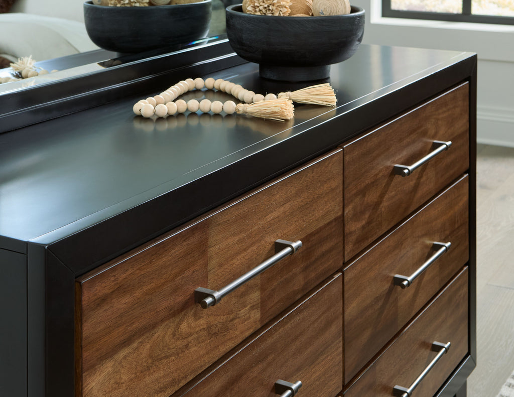 Brown wood dresser front detail with black top, three drawers and silver bar handles