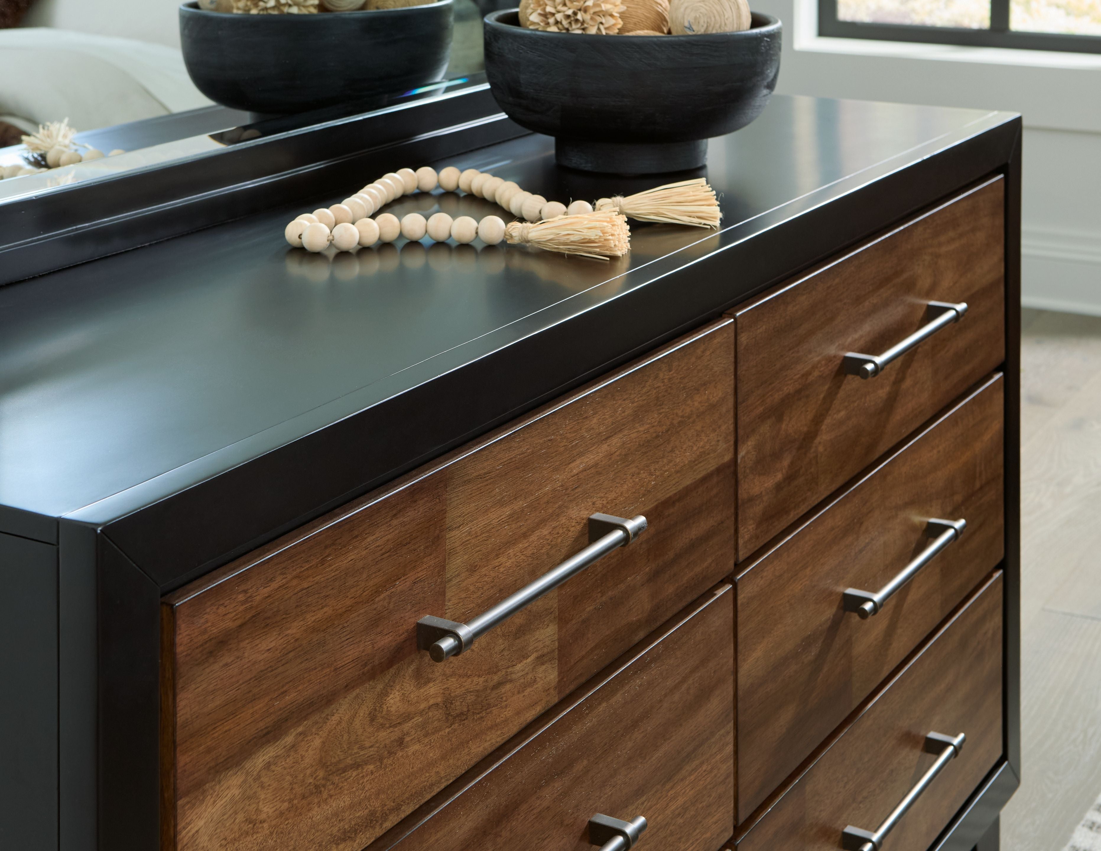Brown wood dresser front detail with black top, three drawers and silver bar handles