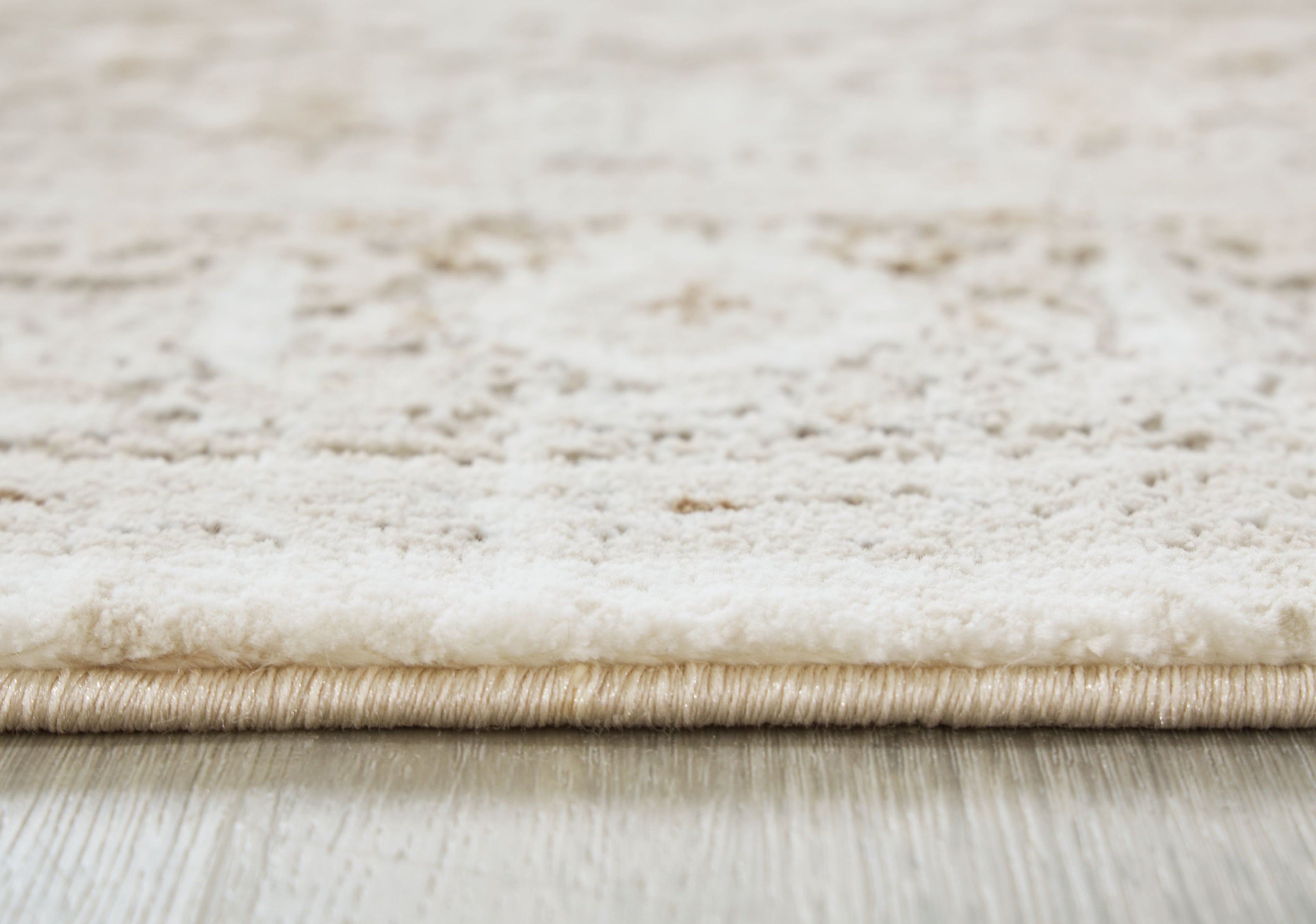 Beige rug pile close-up with bound edge and subtle distressed texture