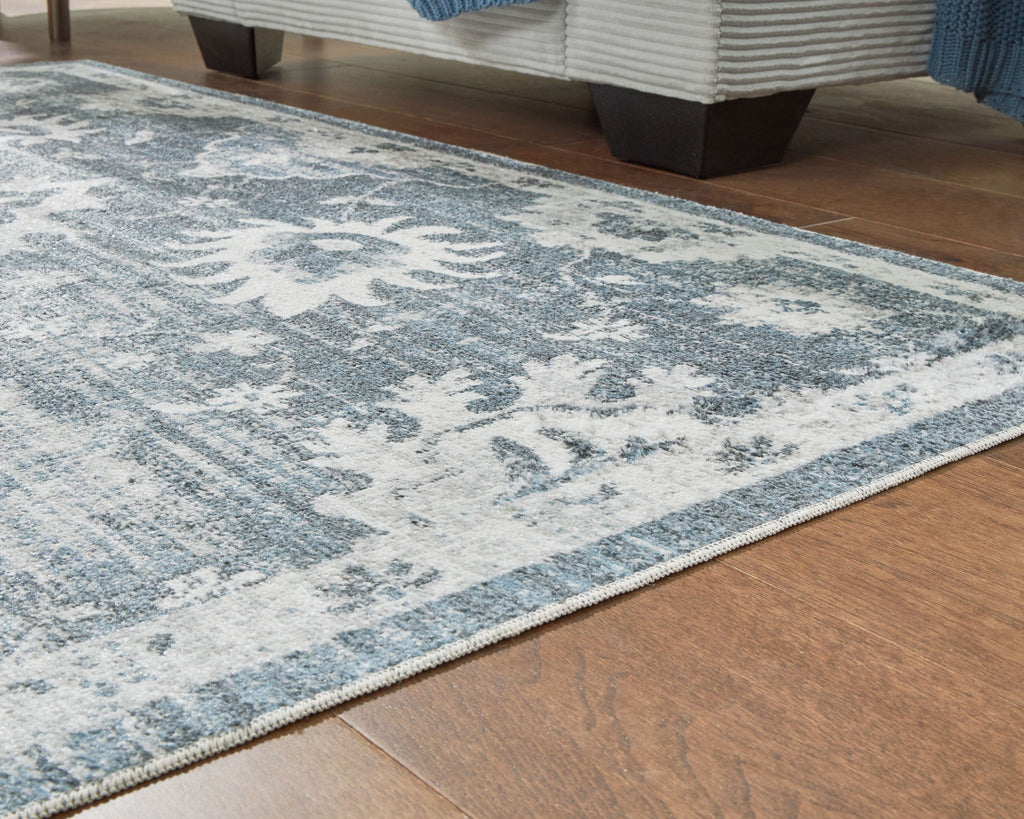 Edge of gray washable rug with blue-gray distressed floral pattern and border