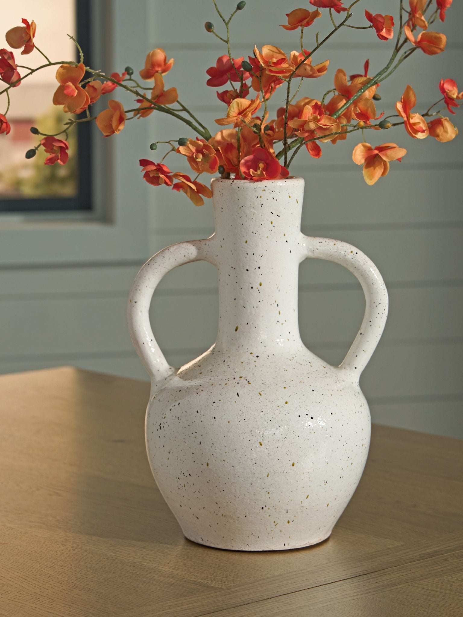 Speckled white ceramic vase with red flowers, two loop handles, and narrow neck.
