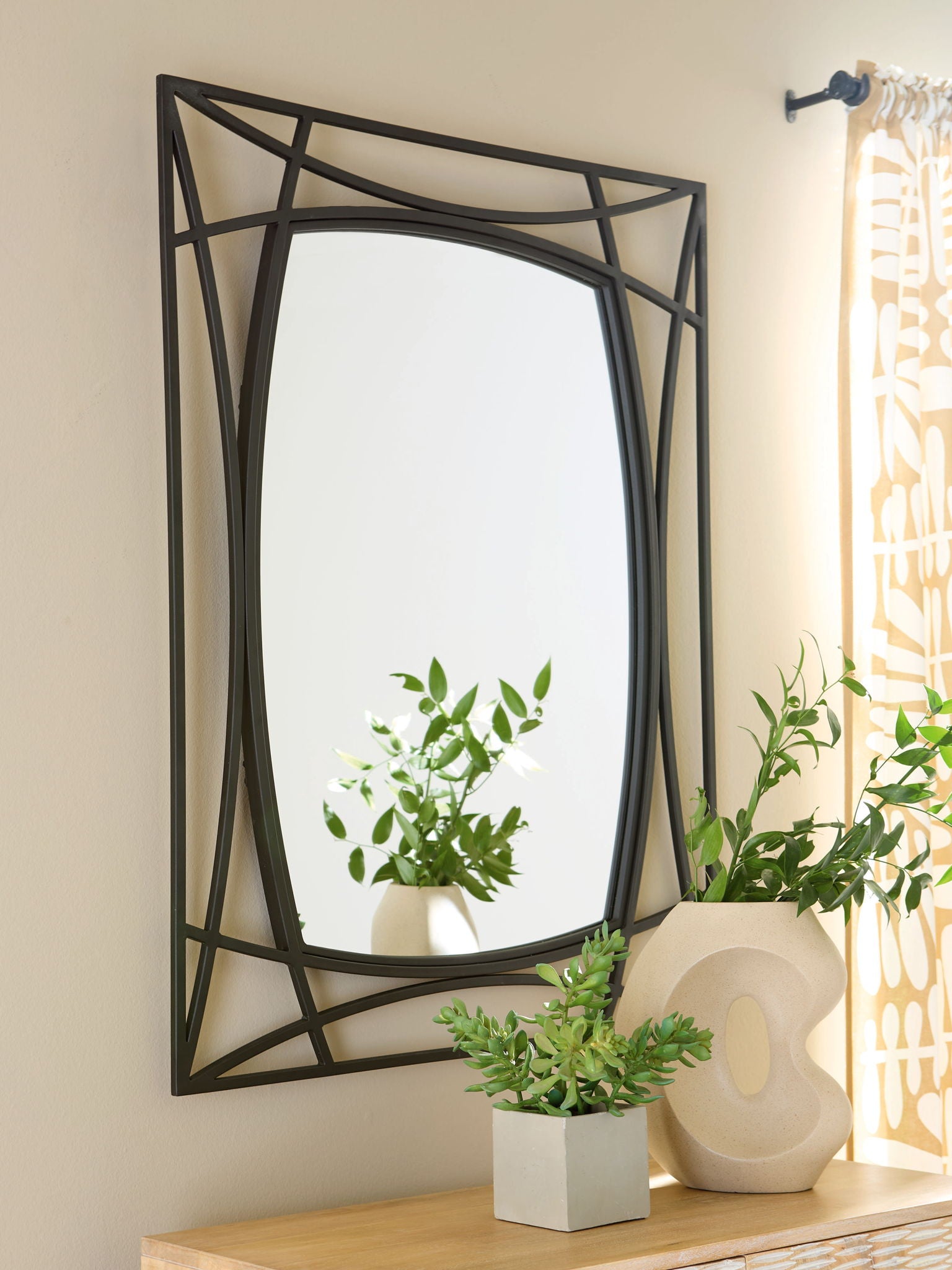 Black accent mirror with geometric frame on wall, with plants on nearby console