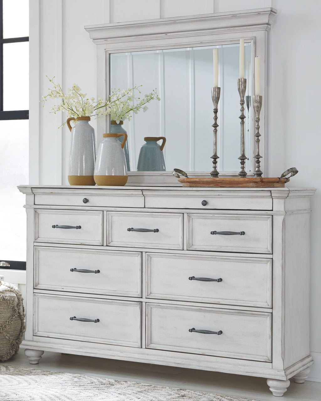 White wood dresser with paneled sides, multiple drawers, and metal bar pulls on top.