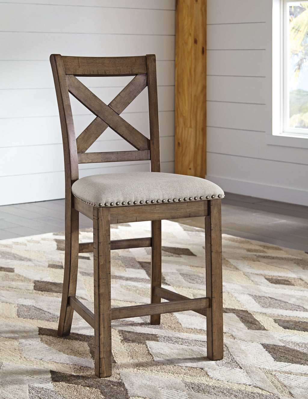 Counter height barstool showing dark wood X-back and beige round upholstered seat with nailheads
