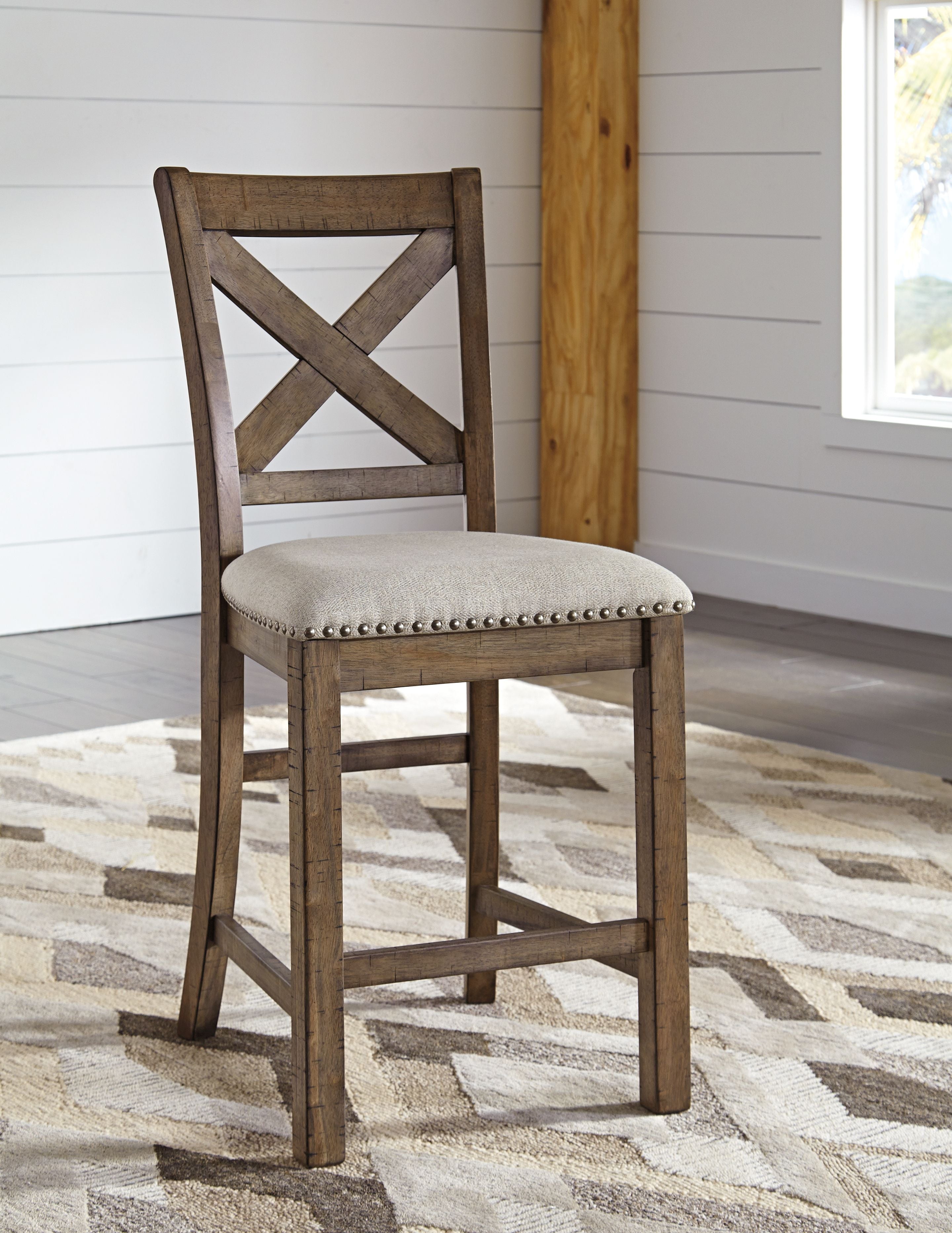 Counter height barstool showing dark wood X-back and beige round upholstered seat with nailheads