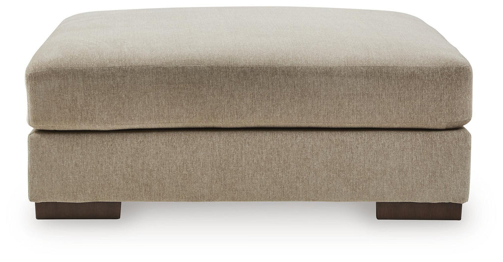 Oversized accent ottoman with padded rounded top in dune beige and short block legs.