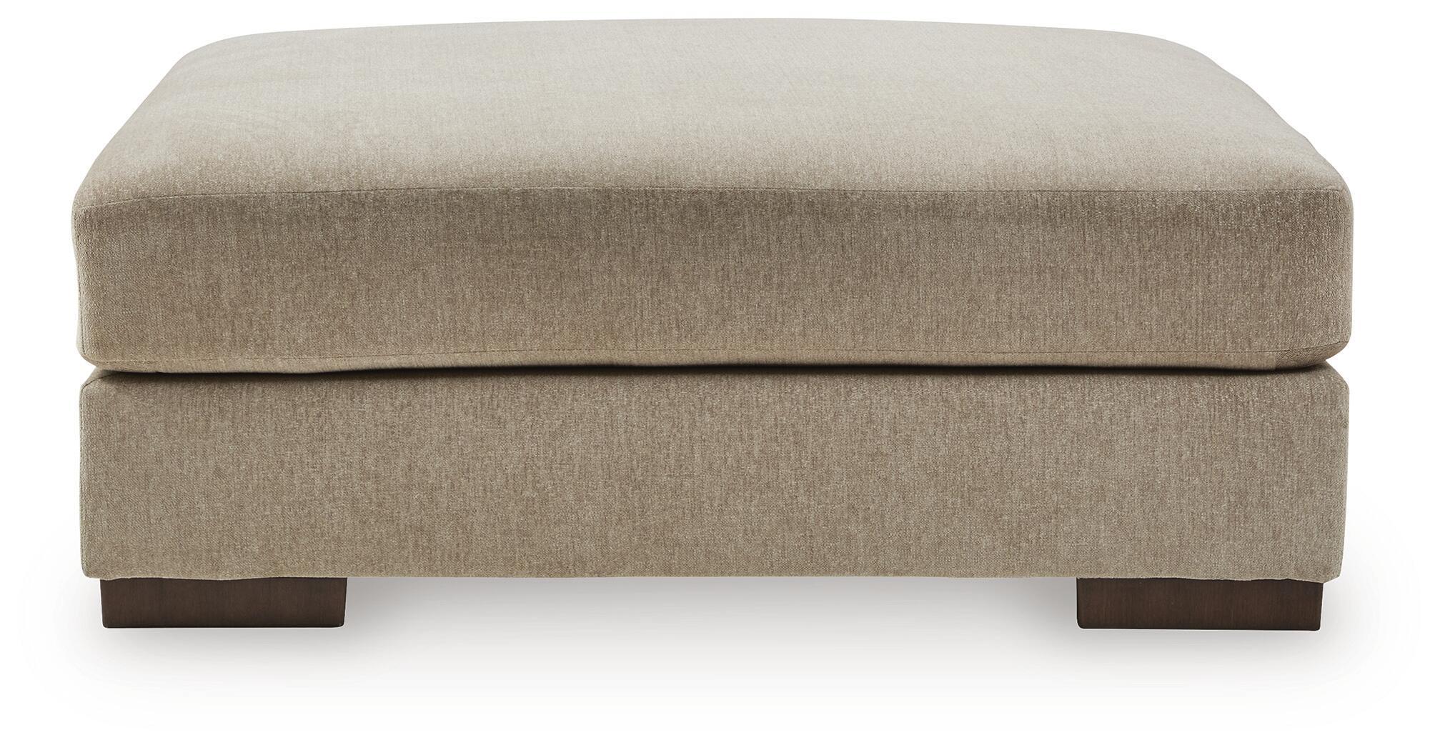 Oversized accent ottoman with padded rounded top in dune beige and short block legs.