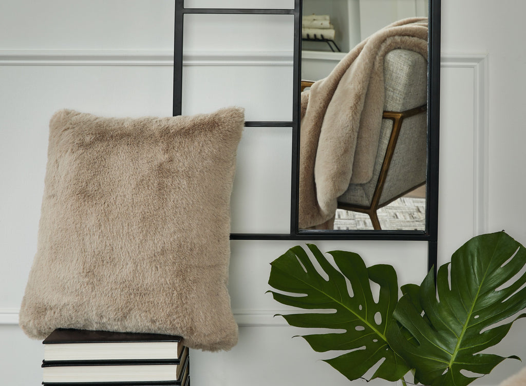 Beige faux fur square pillow with fluffy trim, placed upright on a shelf.