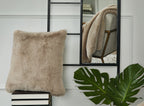 Beige faux fur square pillow with fluffy trim, placed upright on a shelf.