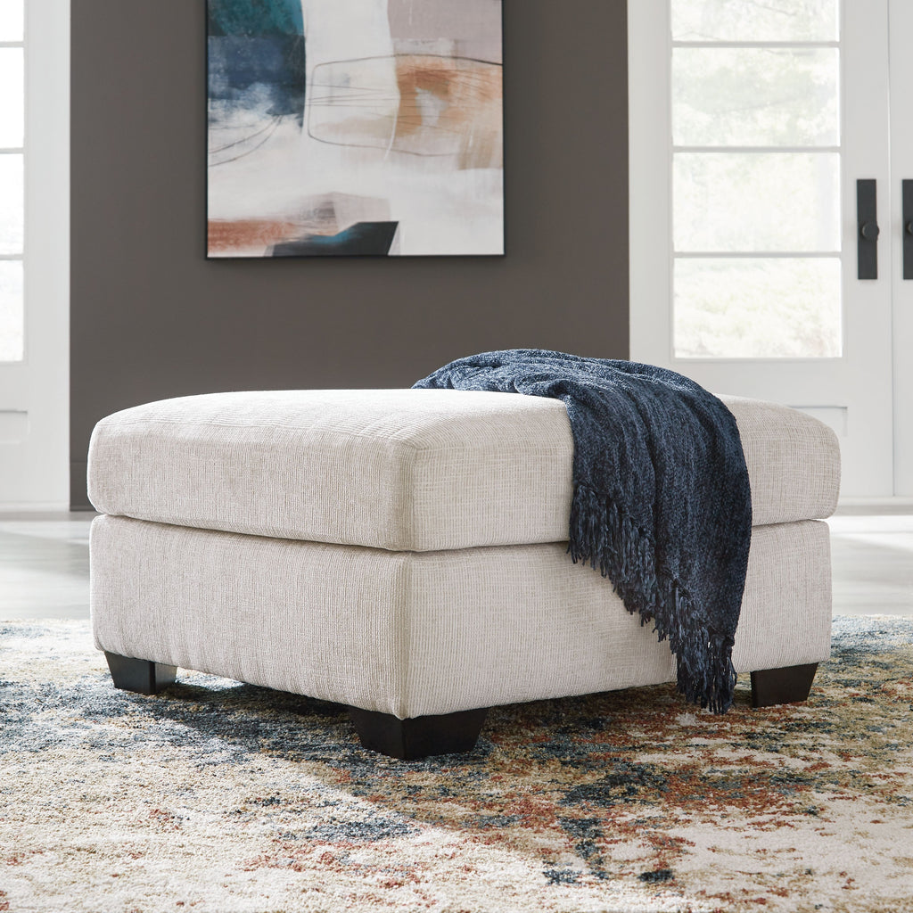 Light cream upholstered ottoman with square arms and dark base legs; includes blue throw.