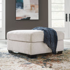 Light cream upholstered ottoman with square arms and dark base legs; includes blue throw.