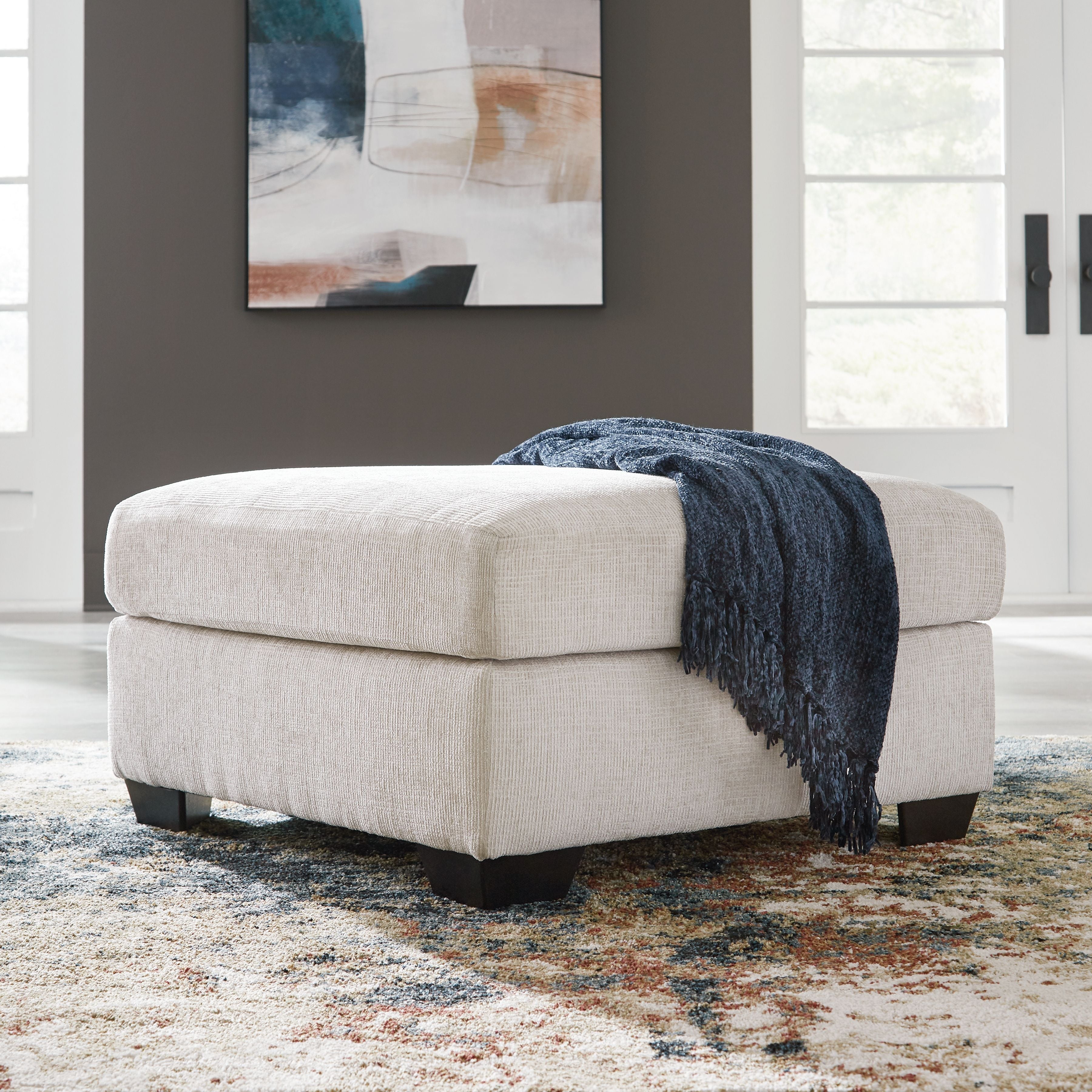 Light cream upholstered ottoman with square arms and dark base legs; includes blue throw.