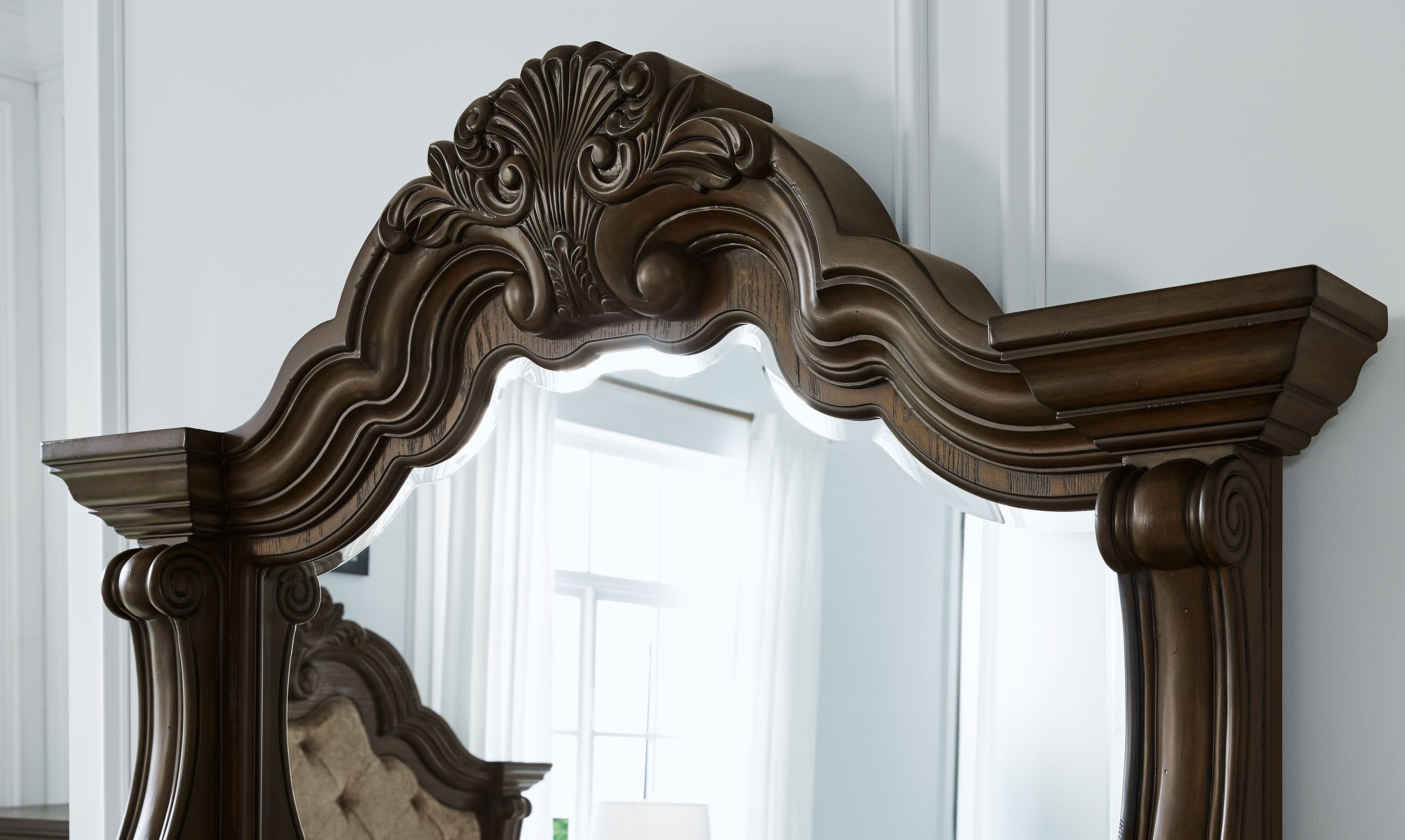 Dark brown arched mirror frame with carved scrollwork and crest detail