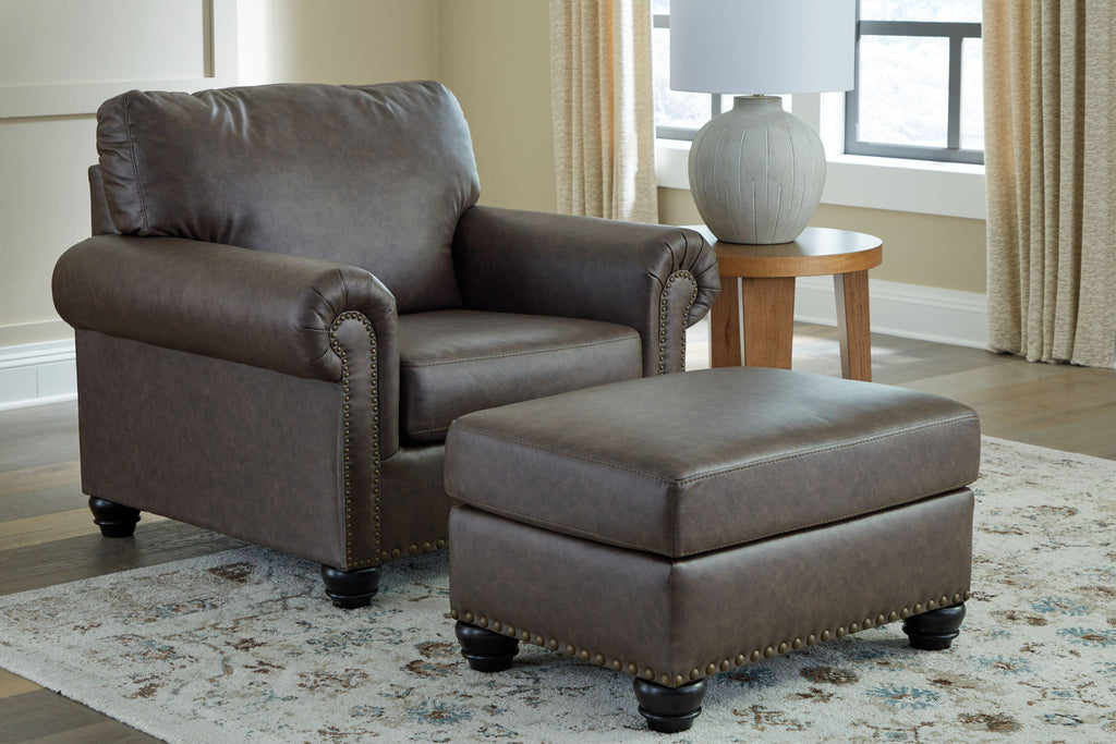 Dark brown upholstered sofa with matching ottoman and nailhead-trim arms.