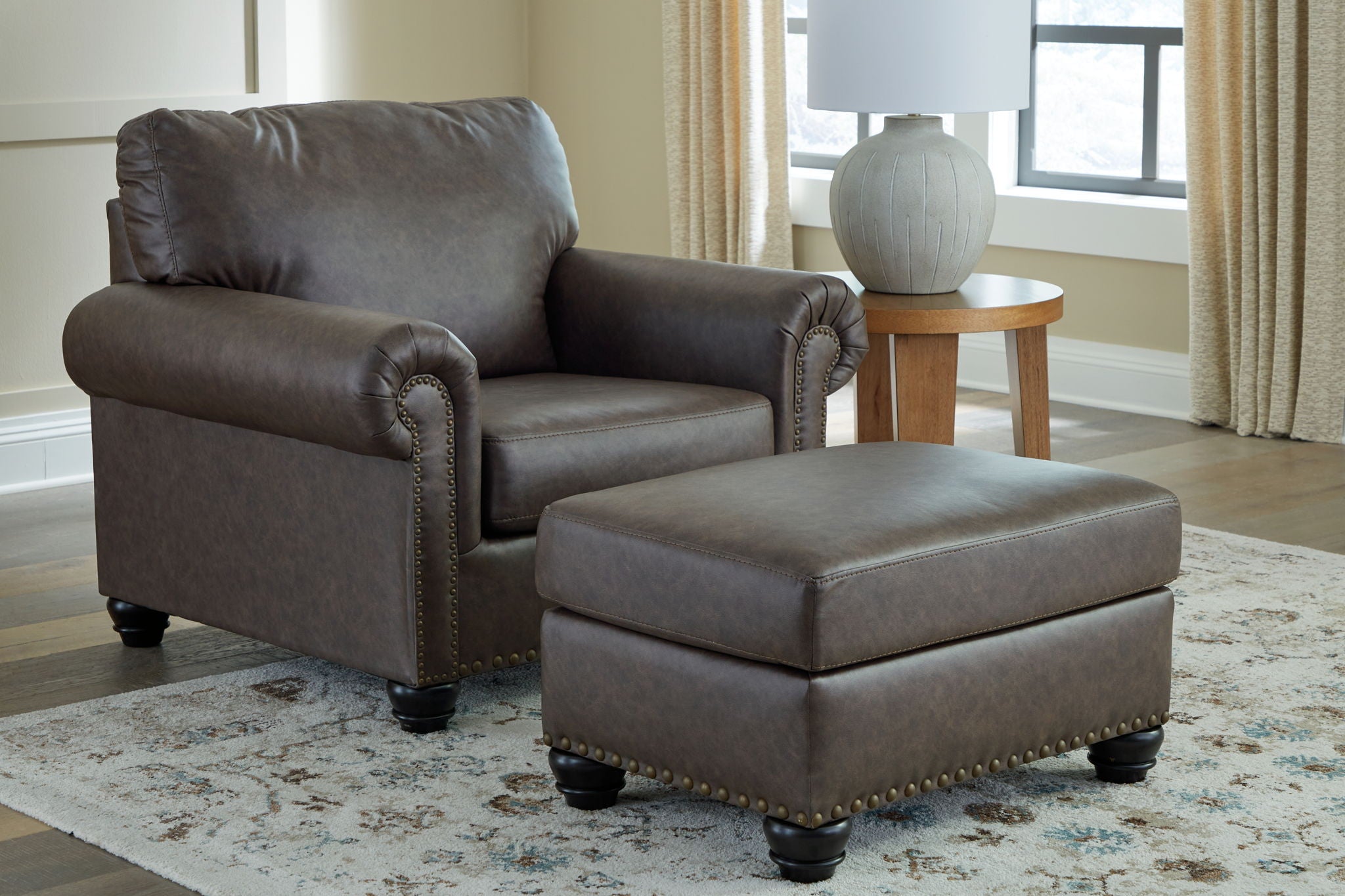 Dark brown upholstered sofa with matching ottoman and nailhead-trim arms.