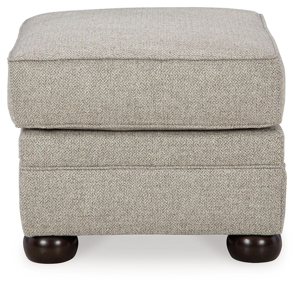 Light beige upholstered ottoman with padded top, stitched panels, and dark wooden legs