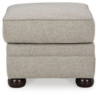 Light beige upholstered ottoman with padded top, stitched panels, and dark wooden legs
