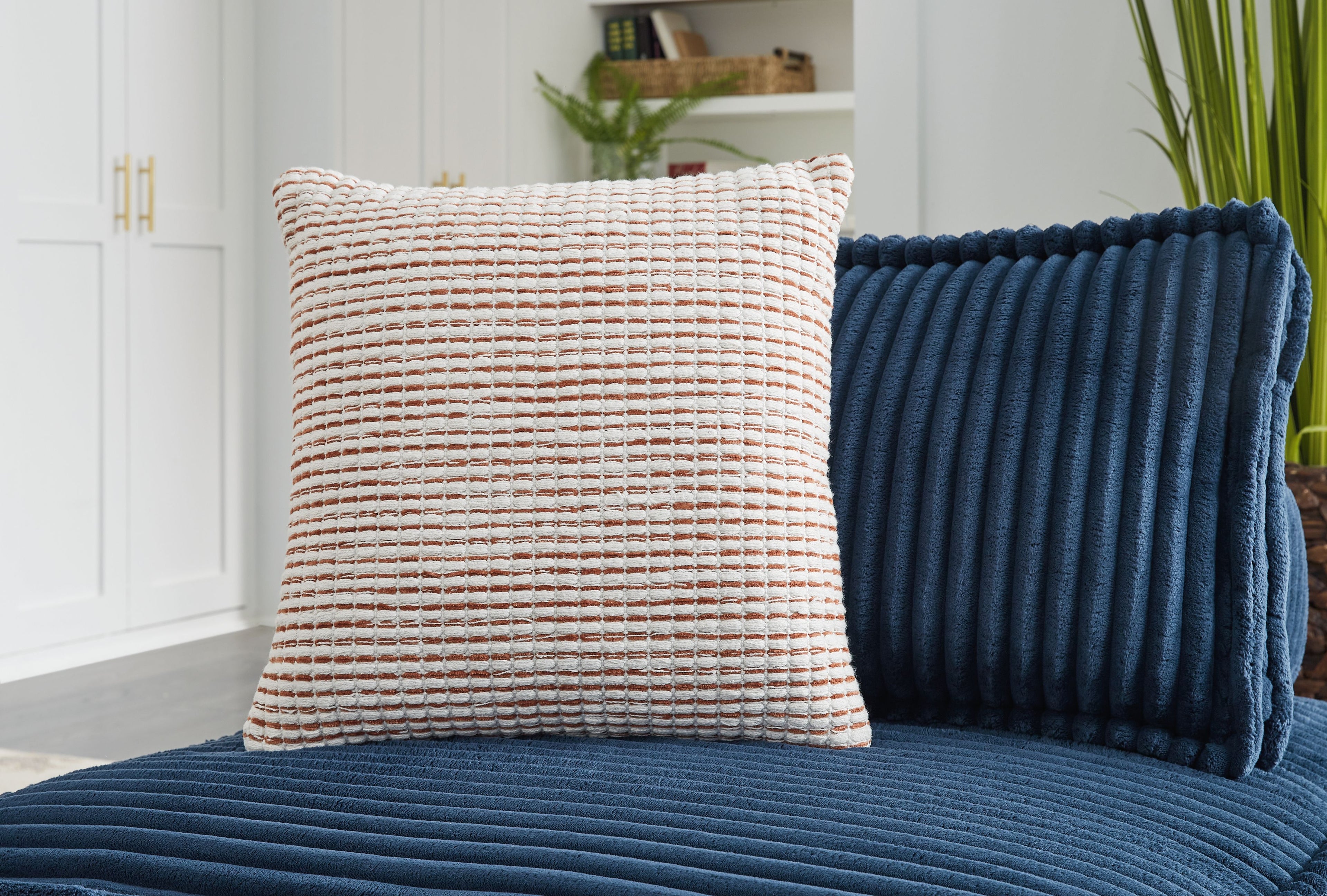 Woven square pillow with red-and-white stripe pattern, shown on a bed