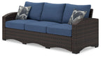 Outdoor sofa with blue cushions, brown wicker arms, two patterned throw pillows