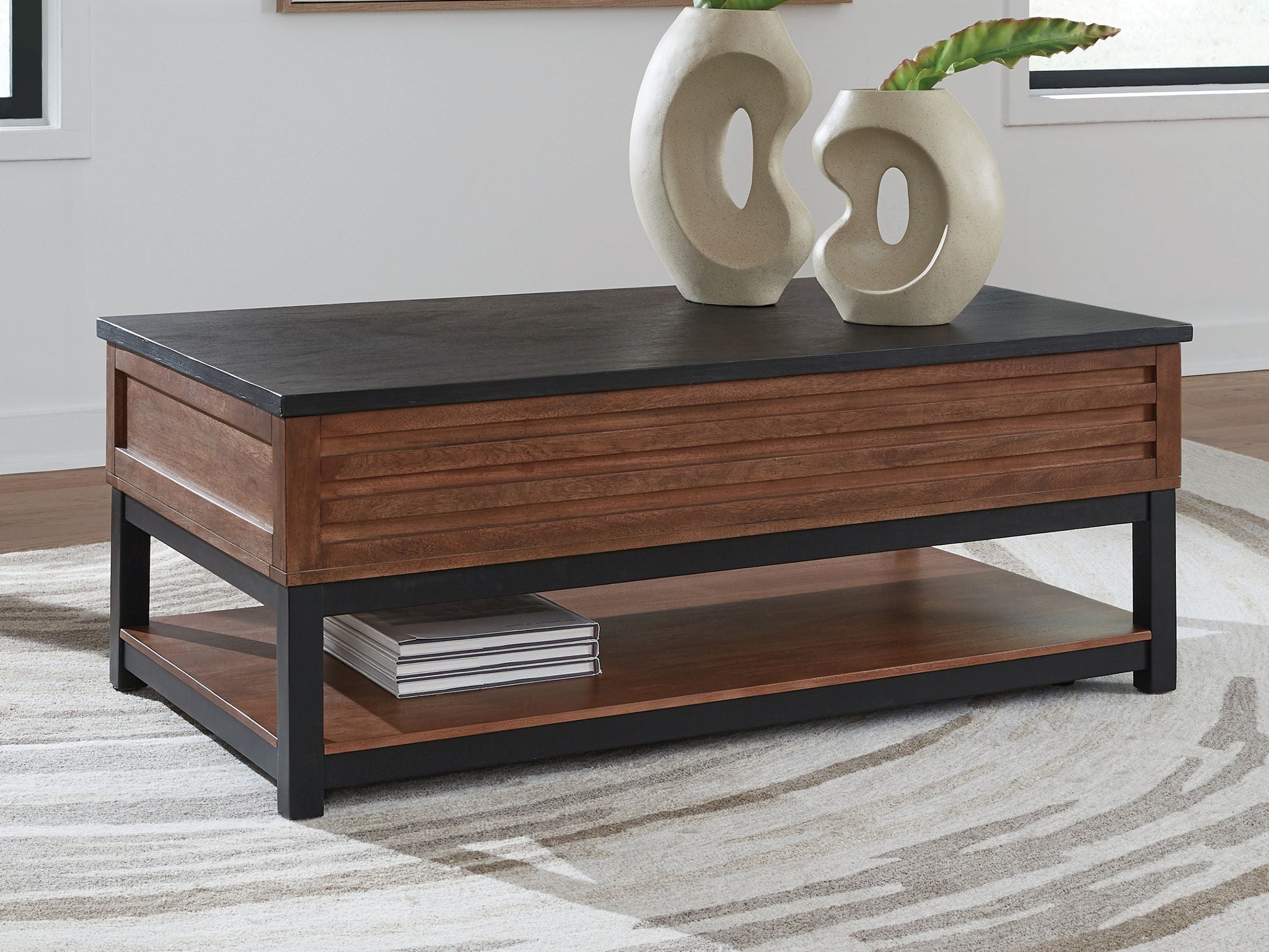 Lift-top cocktail table with dark top, warm brown wood drawers, black base, lower shelf.
