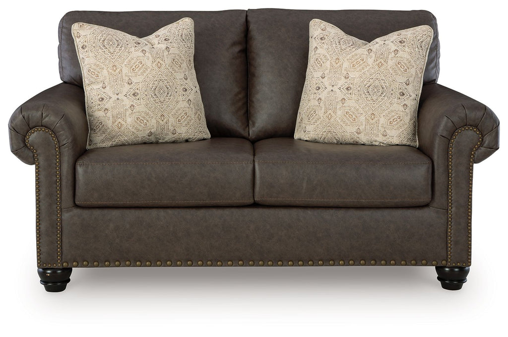 Umber loveseat with tufted arms, nailhead trim, and two patterned throw pillows
