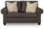 Umber loveseat with tufted arms, nailhead trim, and two patterned throw pillows