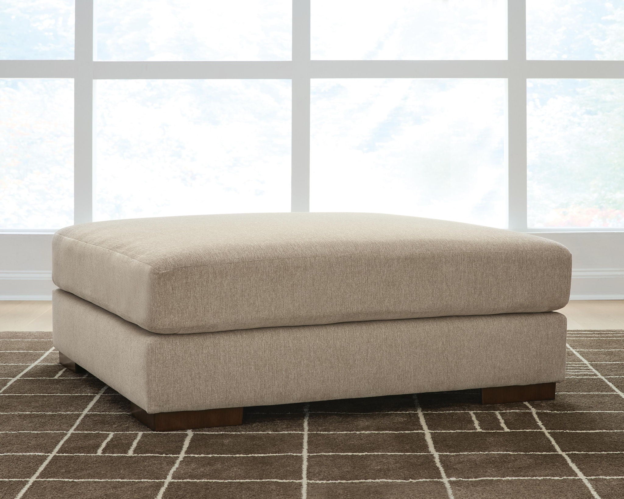 Oversized accent ottoman in dune beige with rounded lid, upholstered sides, and dark feet.
