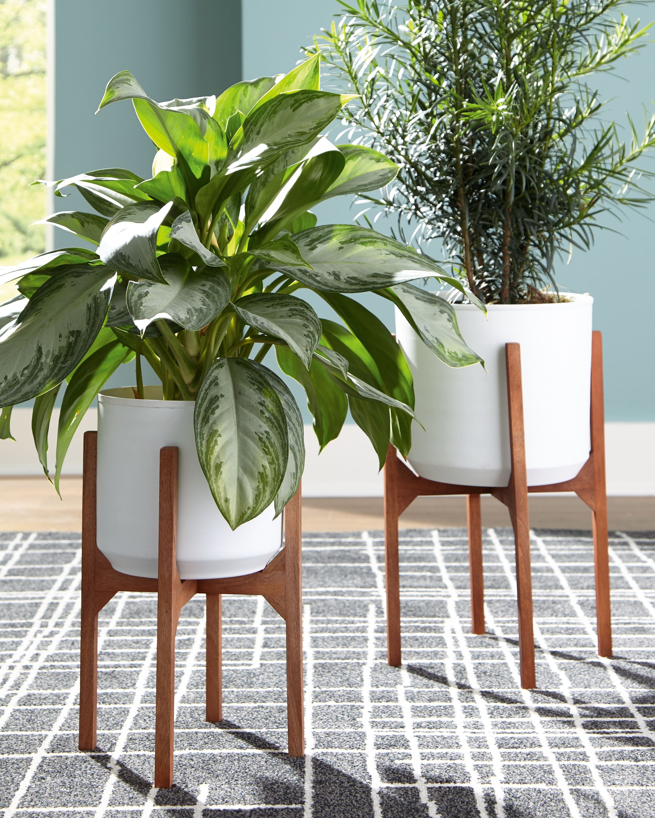 Two white planters on brown wooden stands with potted greenery