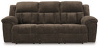 Reclining sofa in dark brown fabric with tufted back panel and wide padded arms