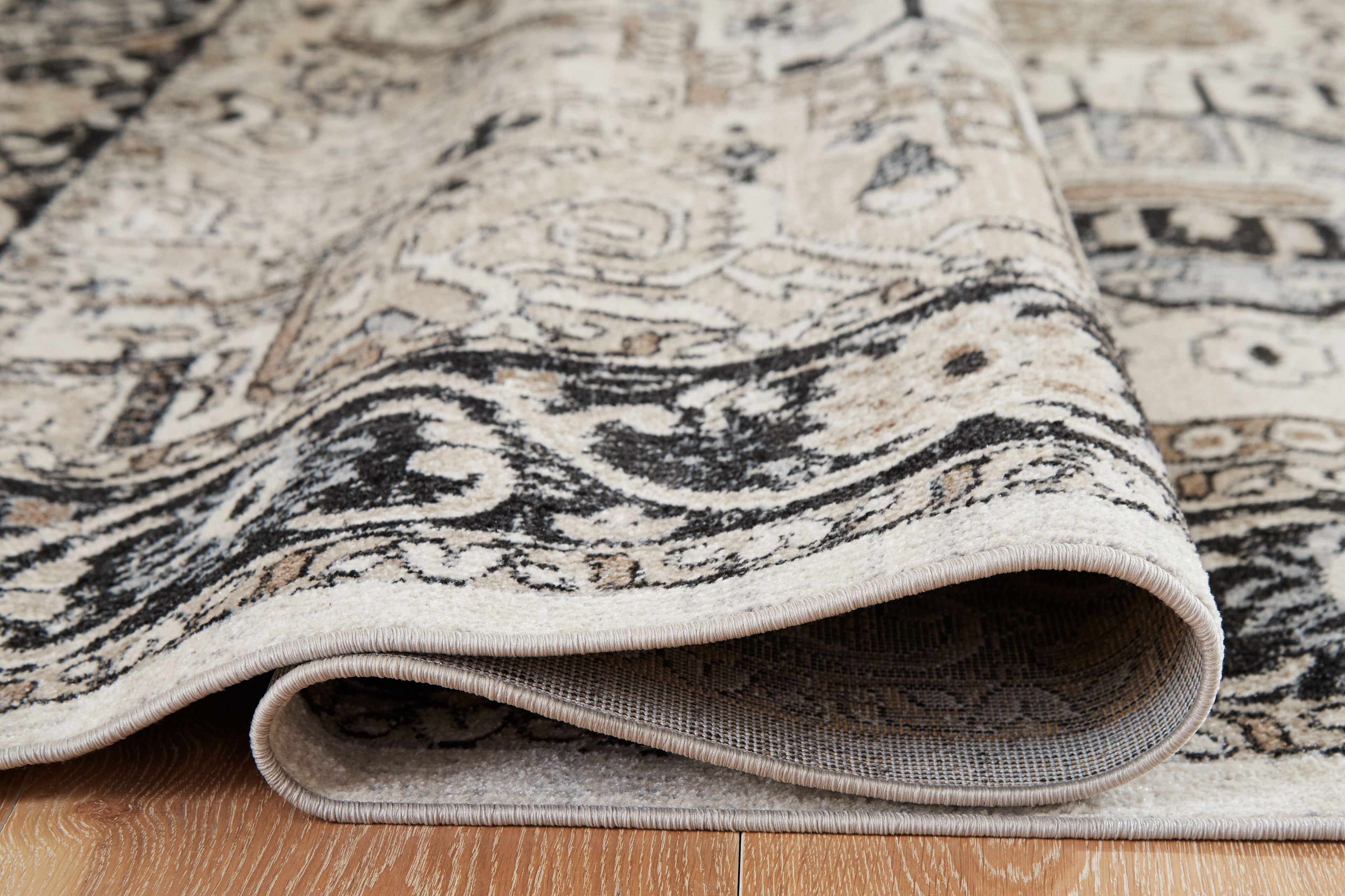 Area rug edge with beige binding on cream and gray base, black ornamental lines
