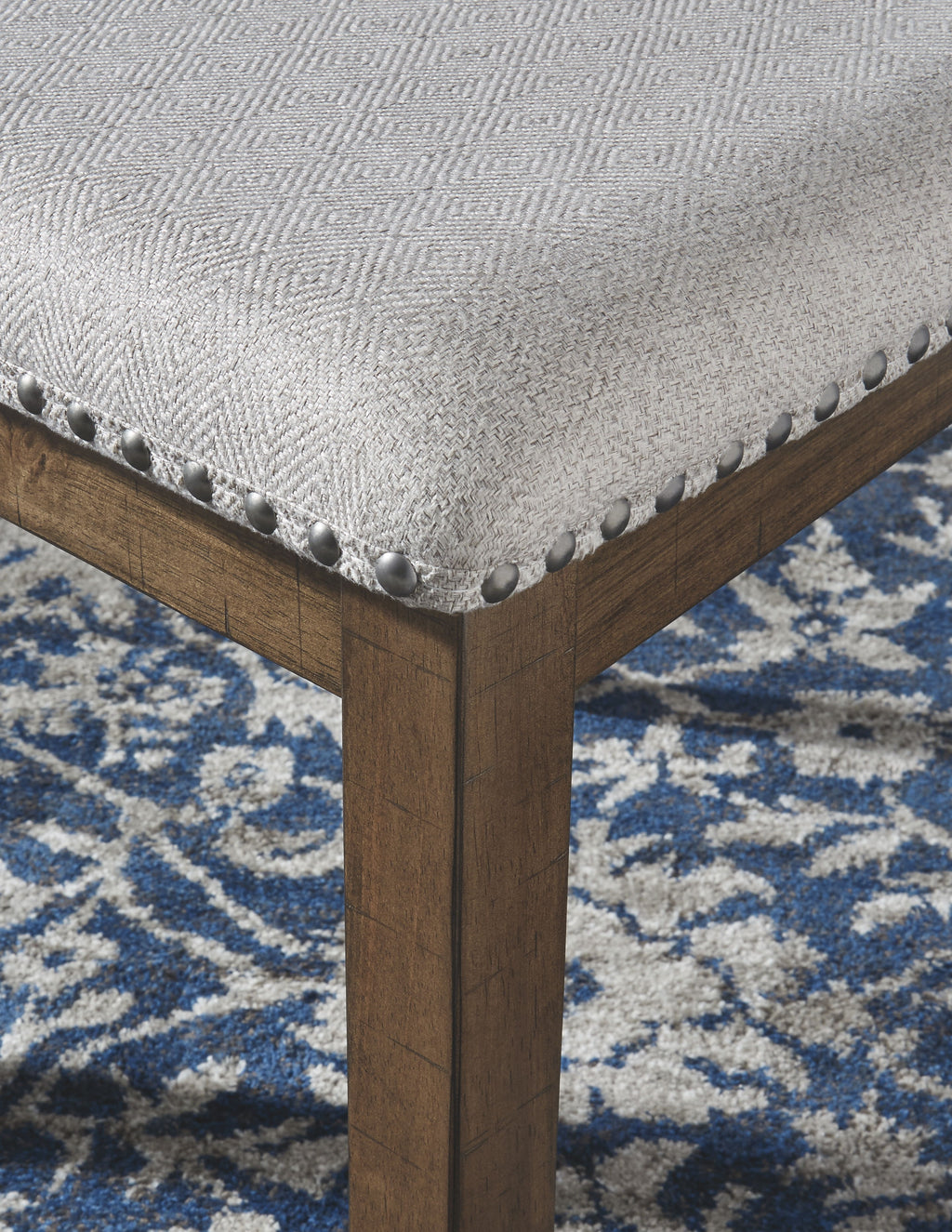 Dining chair corner detail: light upholstered cushion with nailhead trim on dark wood