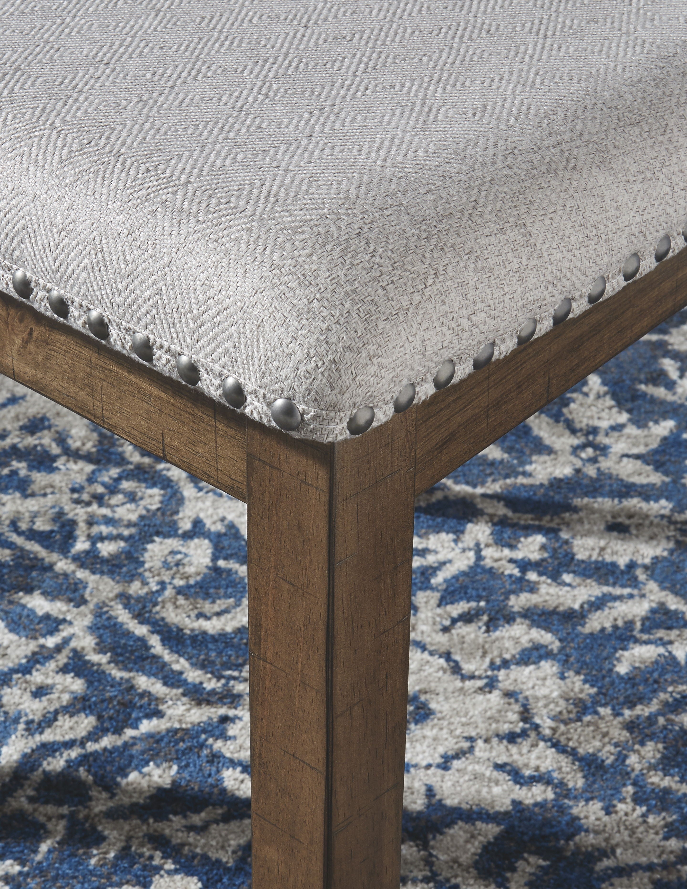 Dining chair corner detail: light upholstered cushion with nailhead trim on dark wood