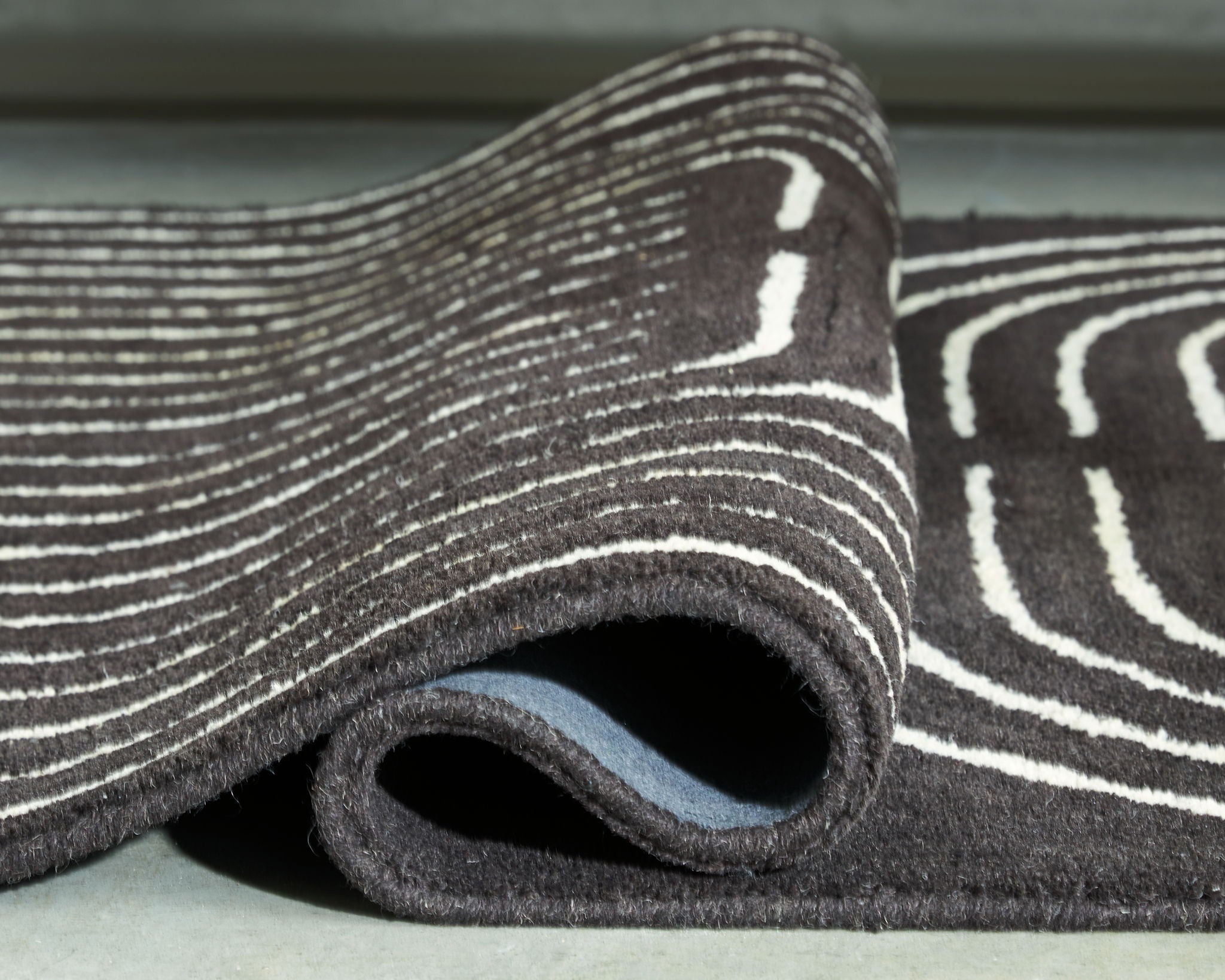 Eldonmore rug close-up: dark pile with white outline stripe pattern on edge.