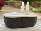 Beige round tabletop on dark brown wicker cocktail table with low, rounded rectangular form