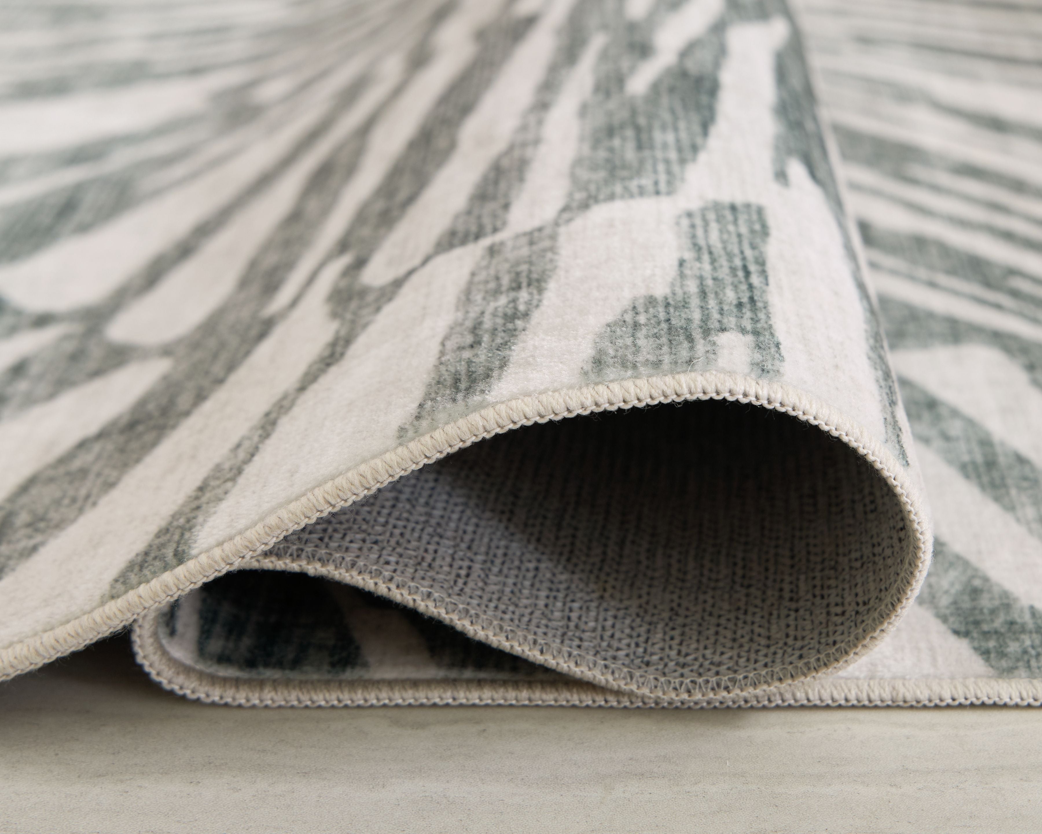 Washable rug corner showing rolled edge; gray sunburst pattern on light background