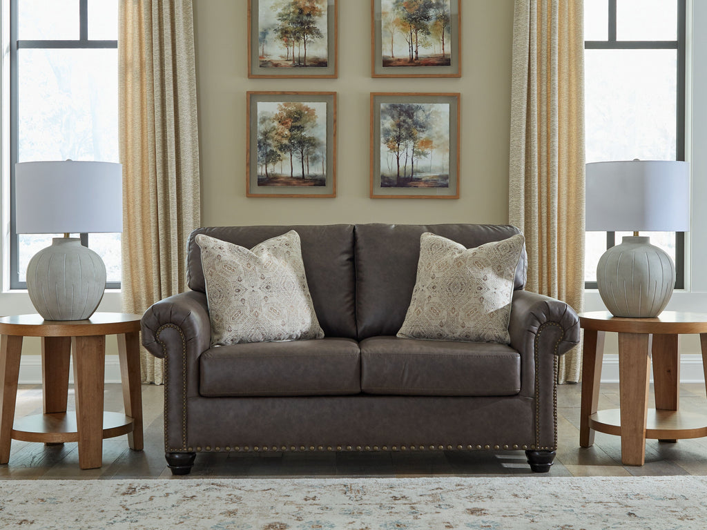 Umber loveseat front view with tufted arms, nailhead trim, and two patterned throw pillows