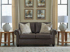 Umber loveseat front view with tufted arms, nailhead trim, and two patterned throw pillows